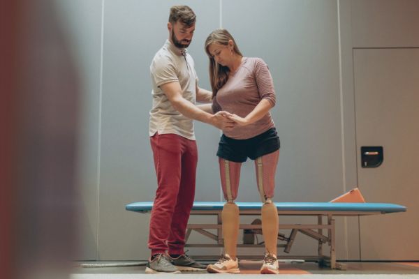 Man standing beside woman with two prosthetic legs helping with balance